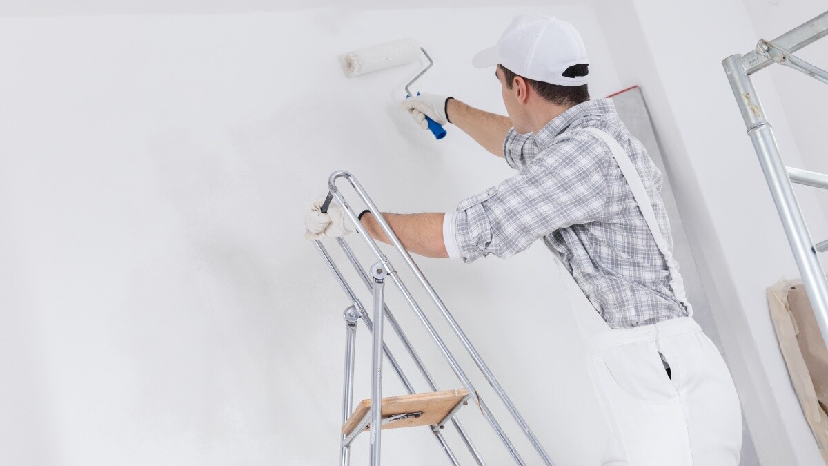 man wearing overalls painting white walls