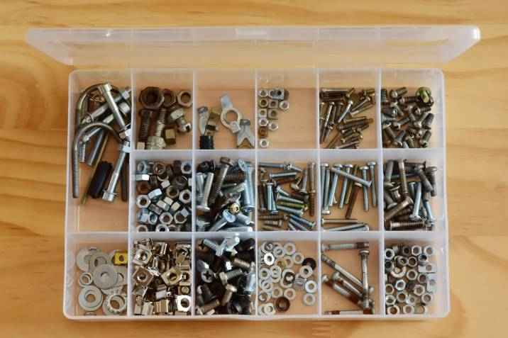 Plastic transparent organiser with various bolts nuts on a wooden surface