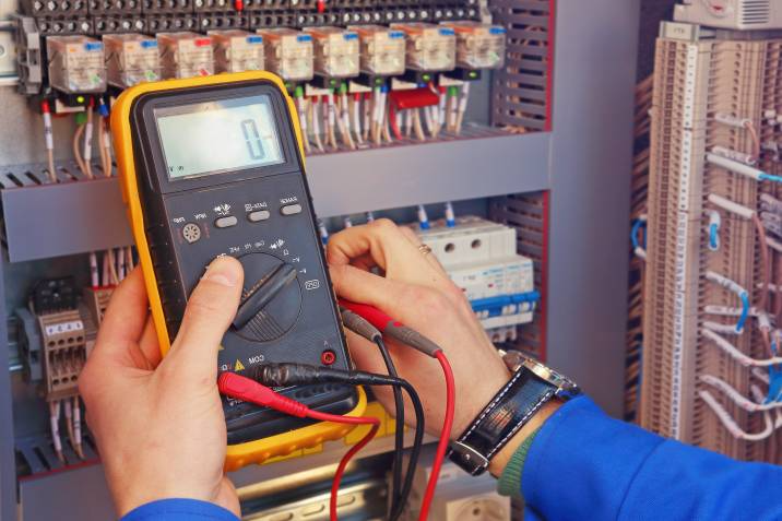 An electrical meter in the hands of an electrician testing a control cabinet 