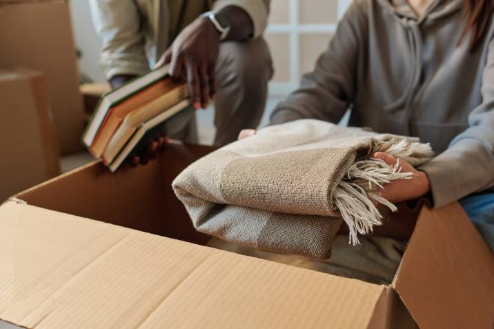 couple packing blanket with books into moving box, using blanket as cushioning to save space 